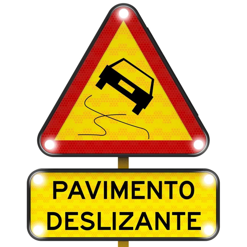 Señal triangular de advertencia con borde rojo y luces blancas que muestra un auto derrapando y la leyenda pavimento deslizante.