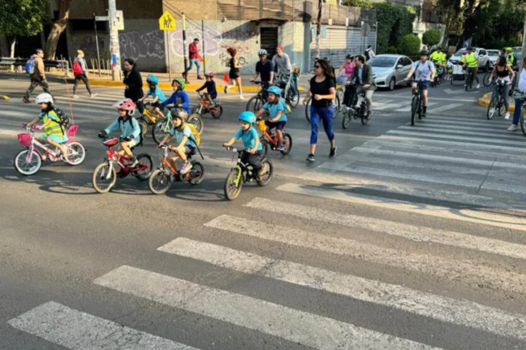 Niñas y niños participando en un Bicibús mientras cruzan la calle rumbo a la escuela acompañados por familias y voluntarios.
