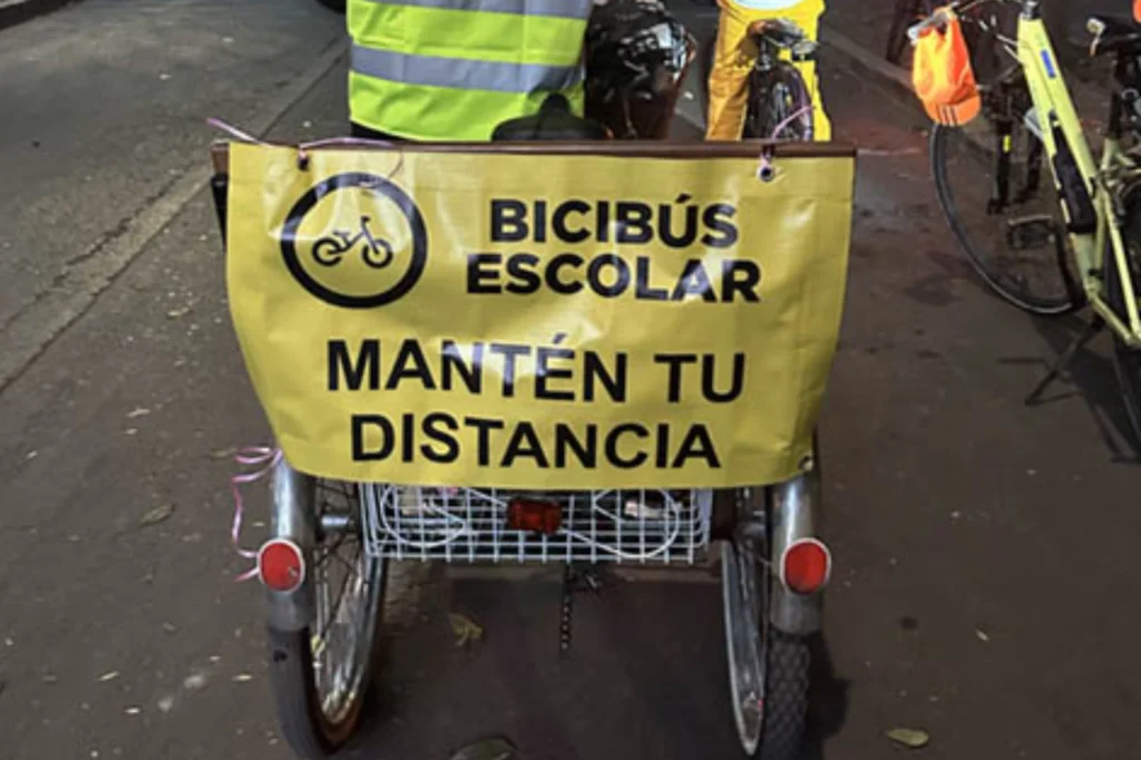 Triciclo con lona de campaña escolar en bicicleta que invita a mantener distancia durante el recorrido de niñas y niños.