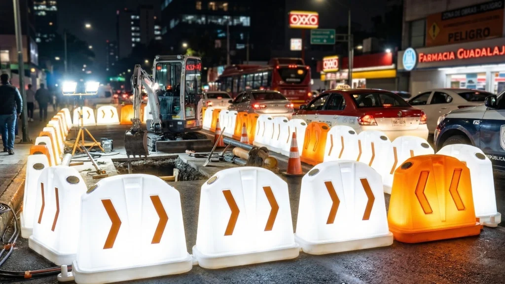 Línea de barreras con luz delimitando carril en vialidad urbana durante la noche